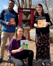 Three team members smiling and holding books.